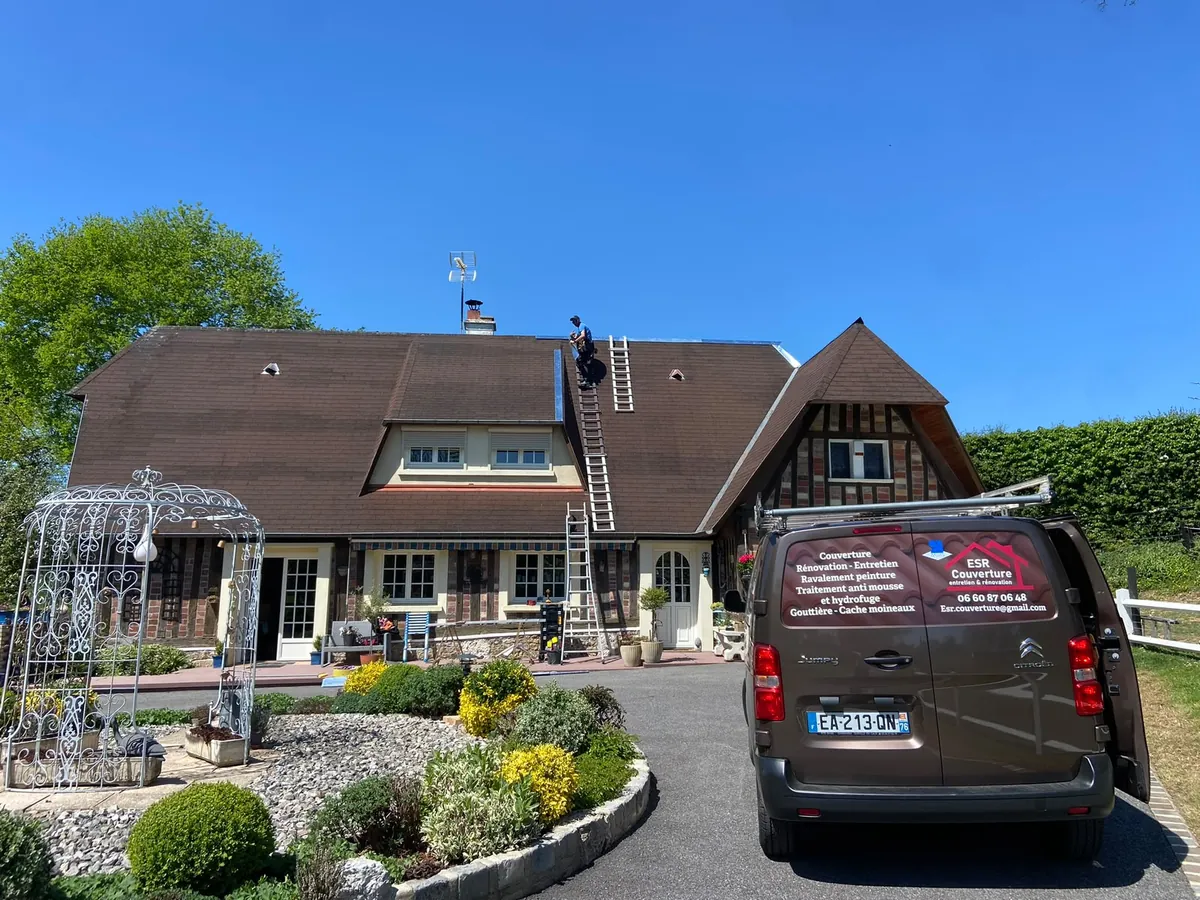 Camion ESR Couverture devant une maison normande à colombages, couvreur au travail sur le toit
